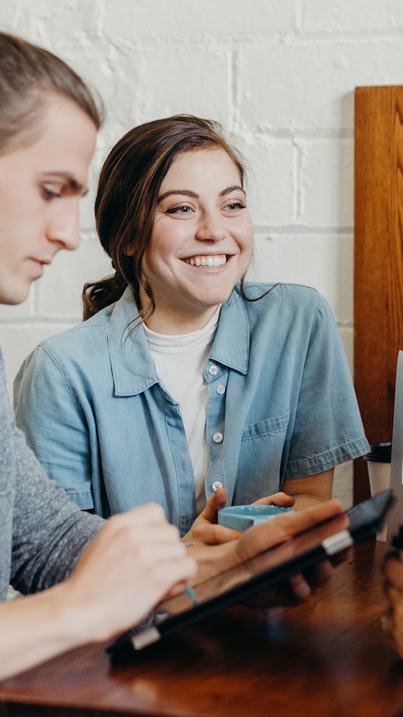Colleague laughing over a coffee at a shared desk during a morning catch-up