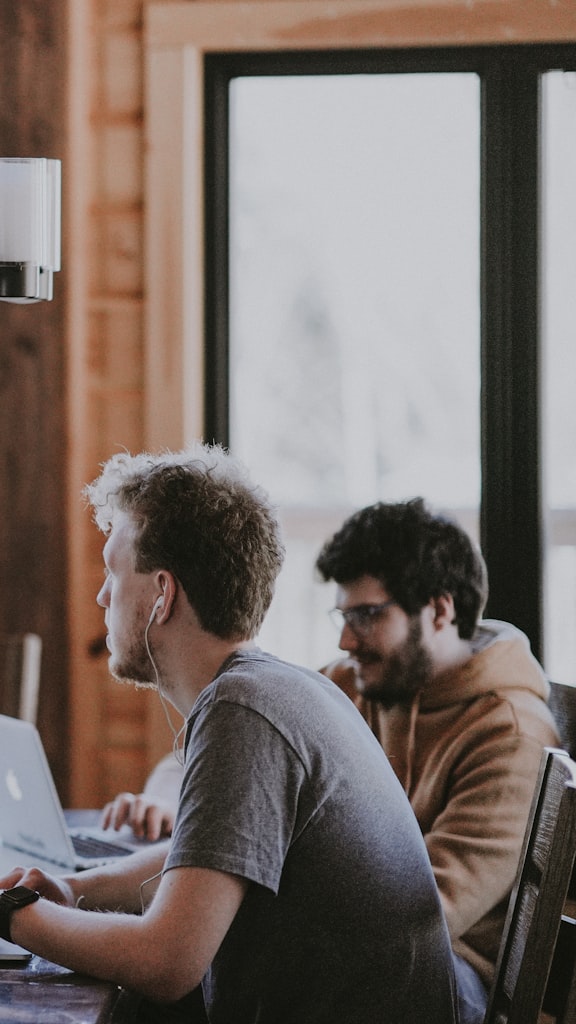 Two coworkers heads-down on laptops beside a big window